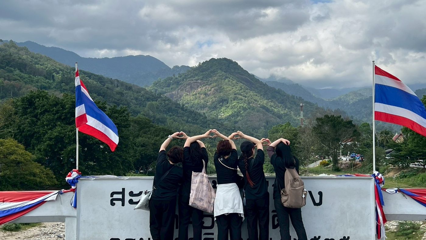 タイの山あいの景色を背にハートをつくるメンバー