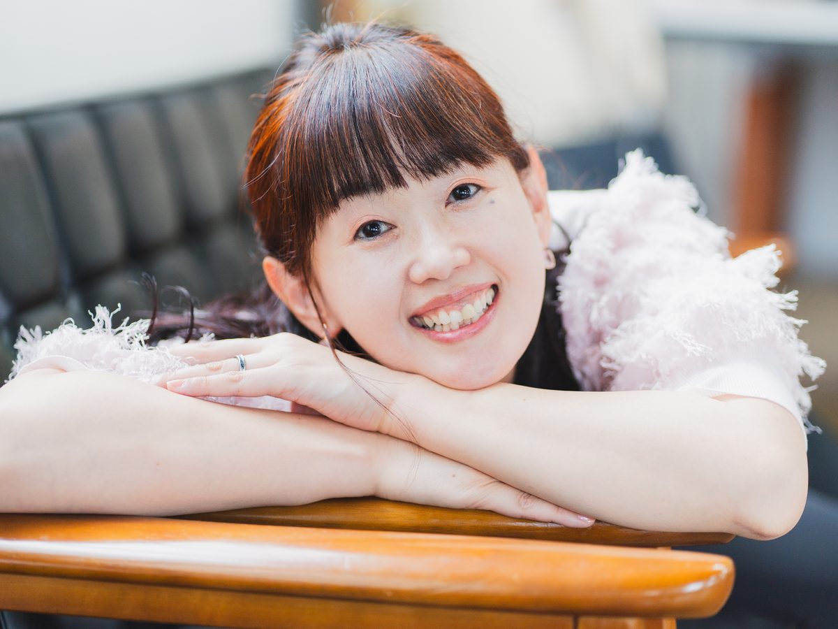 テーブルにひじをついてやわらかく笑うまゆみん